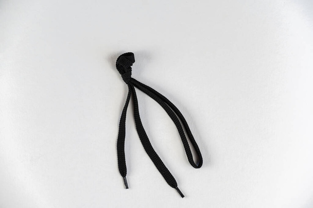 Black lace against a neutral background. Flat shoelace with tied knot. Close-up. Selective focus. - Photo, Image
