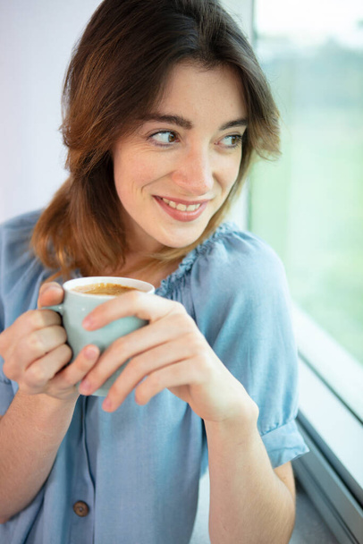 woman drinking coffee at home next to window - Foto, Imagen
