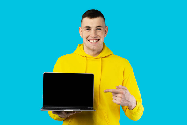 Happy Freelancer Guy Mostrando Laptop Tela Vazia Publicidade Site Apontando o dedo para o computador e sorrindo para a câmera posando sobre fundo azul, Studio Shot. Tecnologia da Internet e E-Learning - Foto, Imagem
