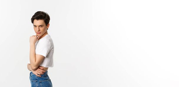 Lgbtq and pride concept. Side view of attractive androgynous man in crop top looking sassy at camera, standing over white background. - Foto, Imagem
