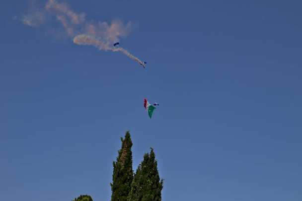 Un paracaidista militar lanzado desde un helicóptero desenrolla la bandera italiana, en un día de la república italiana. - Foto, imagen