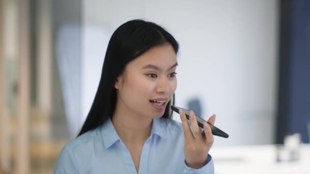 Moderno concetto di comunicazione. Giovane donna asiatica positiva che registra messaggi vocali agli amici, che parla con l'app mobile sullo smartphone, in piedi in ufficio, rallentatore - Filmati, video
