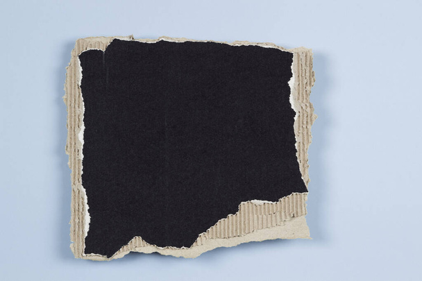 Прямокутний шматок чорного гофрованого картону з рваними краями на світло-блакитному фоні. Вид зверху, простір для копіювання
. - Фото, зображення