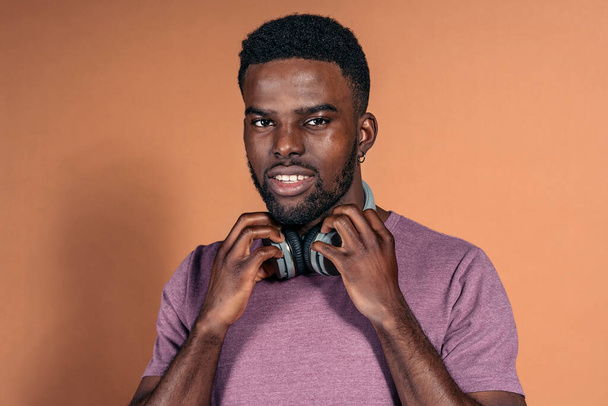 Stock photo of handsome black man wearing headphones looking at camera in studio shot against brown background. - Photo, Image