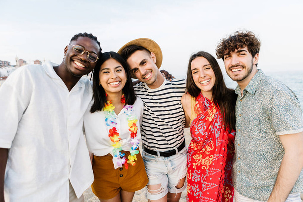 Ryhmäkuva monirotuisista nuorista ystävistä ulkona kesällä - United five millennial people halaa toisiaan hymyillen kameran edessä bilerannalla - Valokuva, kuva