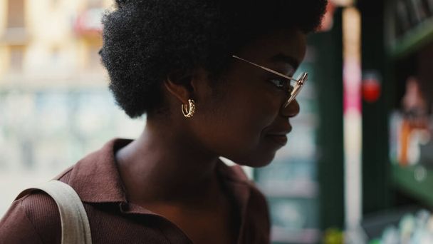 Side view of an African girl in glasses smiling outdoors. Beautiful woman wearing earrings - Photo, Image