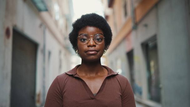 Sakin bir sokakta duran genç Afrikalı kadın. Çekici kaygısız kız kameraya bakıyor, gözlük takıyor. - Fotoğraf, Görsel