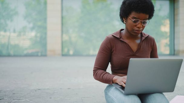 freelancer mujer que trabaja en el ordenador portátil al aire libre. Hermosa mujer Afro estudiando durante el descanso en la calle - Foto, Imagen