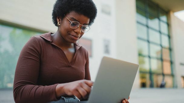 女性起業家がラップトップで屋外で働いています。アフリカ系アメリカ人の女性が路上でラップトップで勉強している - 写真・画像