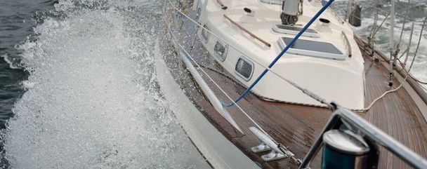 Vieux yacht classique naviguant en pleine mer pendant la tempête. Pont en teck de bois. Ketch voilier. Vagues, éclaboussures d'eau. Croisière, vacances, régate, sport, loisirs - Photo, image
