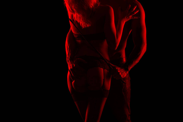 Man holding whip and lover in underwear at night in red light, bdsm - Photo, Image