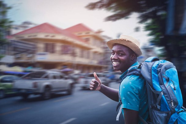 Африканський турист у капелюшках подорожніх рюкзаків, що ходять по міській дорозі з посмішкою і щастям. - Фото, зображення