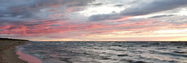 Blick von der Ostseeküste bei Sonnenuntergang. Dramatischer Gewitterhimmel, glühende Wolken, goldenes Sonnenlicht. Wellen, spritzendes Wasser. Natur, Umwelt, unbeständiges Wetter - Foto, Bild