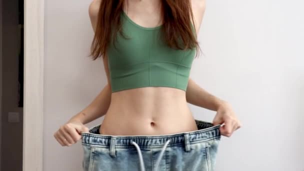 Laihdutetun naisen hoikka ruumis. Nuori tyttö, jolla on ohut vyötärö valtavissa farkuissa laihtumisen jälkeen - Materiaali, video