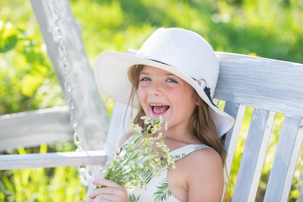 Outdoor small child girl portrait on the meadow. Little cute kid with flowers in a garden. Children play outdoors. Kid play outdoor. Concept of happy childhood and summer leisure - 写真・画像