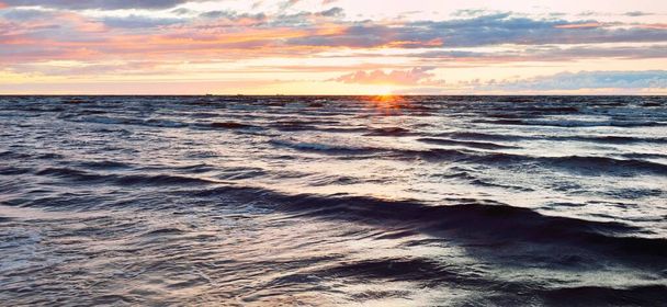 Blick von der Ostseeküste bei Sonnenuntergang. Dramatischer Gewitterhimmel, glühende Wolken, goldenes Sonnenlicht. Wellen, spritzendes Wasser. Natur, Umwelt, unbeständiges Wetter - Foto, Bild