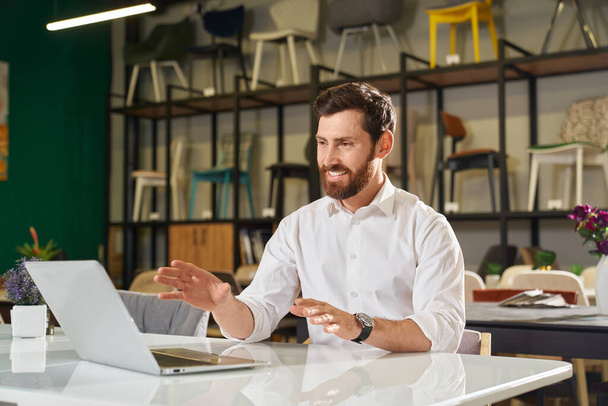 Front view of happy designer, architect sitting at table, working, using laptop. Brunette male with beard looking at screen, smiling, designing. Concept of urban lifestyle. - Foto, imagen