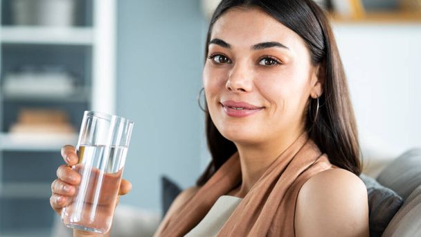 Μια νεαρή γυναίκα πίνει ένα ποτήρι νερό. - Φωτογραφία, εικόνα