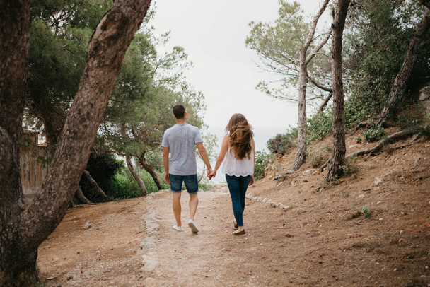 Una foto da dietro di un uomo ispanico e la sua ragazza latina che discendono dal bosco in un parco montuoso in Spagna. Un paio di turisti si stanno divertendo a Valencia - Foto, immagini