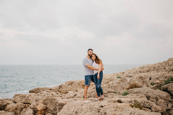 Hiszpan i jego latynoska dziewczyna ściskają się na skalistym wybrzeżu morza w parku góralskim w Hiszpanii. Para turystów cieszy się turystyką w Walencji. - Zdjęcie, obraz