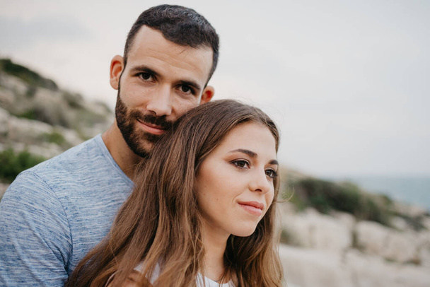 A close portrait of a Hispanic man who is hugging a Latina girl on the rocky sea coast in Spain. A couple of tourists in the evening in a highland park in Valencia. - Fotografie, Obrázek
