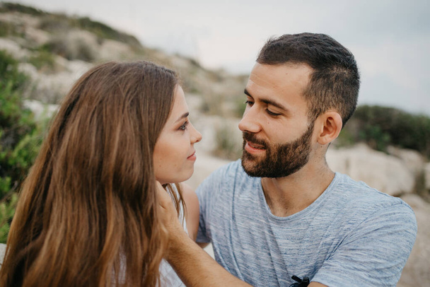 Blízká fotka hispánského muže, který hladí rukama tvář své latinské přítelkyně na skalnatém mořském pobřeží ve Španělsku. Pár turistů večer na kopcích ve Valencii - Fotografie, Obrázek
