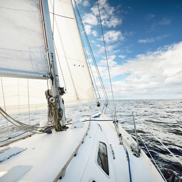Valkoinen sloop peukaloitu jahti purjehtii avomerellä kirkkaana päivänä. Näkymä kannelta keulaan. Cumulus-pilviä. Kuljetus, matkustaminen, risteily, urheilu, virkistys, vapaa-ajan toiminta, kilpa-ajo, regatta - Valokuva, kuva