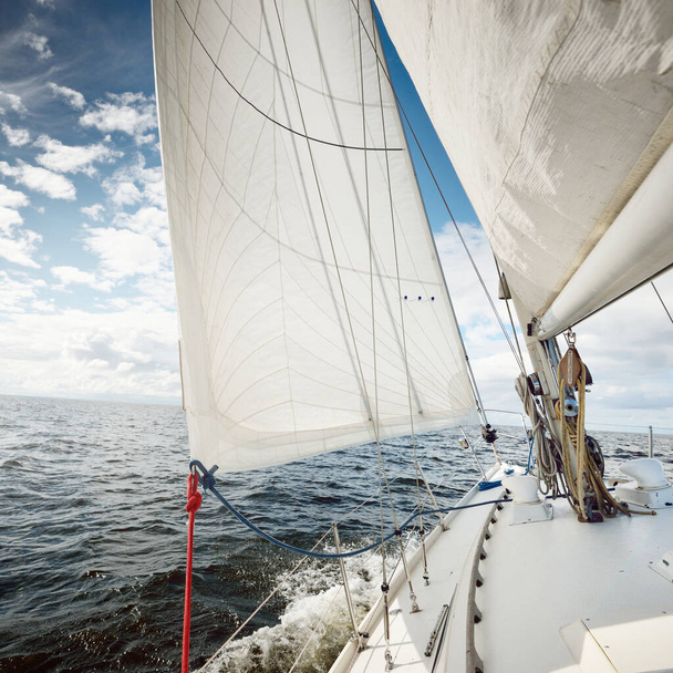 White sloop rigged yacht sailing in an open sea on a clear day. A view from the deck to the bow. Cumulus clouds. Transportation, travel, cruise, sport, recreation, leisure activity, racing, regatta - Photo, Image