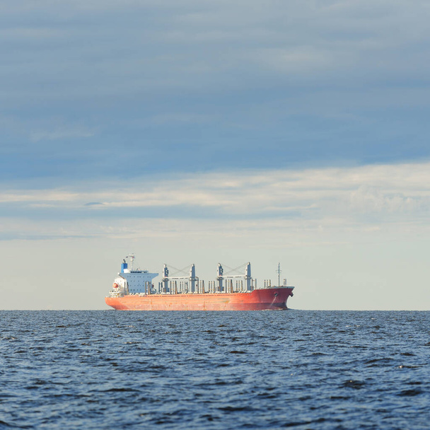 Gran granelero rojo (179 metros de longitud) navegando en un mar Báltico abierto. Cielo dramático. Transporte de mercancías, embarcación náutica, logística, comunicaciones globales, economía, negocios, industria - Foto, imagen