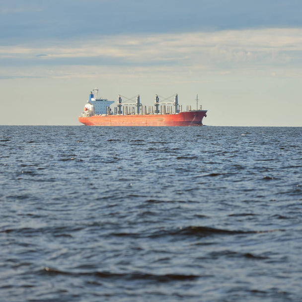 Büyük kırmızı bir yük gemisi (179 metre uzunluğunda) açık bir Baltık Denizi 'nde yüzüyor. Dramatik bir gökyüzü. Yük taşımacılığı, denizcilik gemisi, lojistik, küresel iletişim, ekonomi, iş dünyası, sanayi - Fotoğraf, Görsel