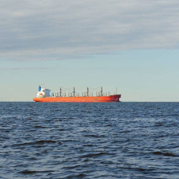 Gran granelero rojo (179 metros de longitud) navegando en un mar Báltico abierto. Cielo dramático. Transporte de mercancías, embarcación náutica, logística, comunicaciones globales, economía, negocios, industria - Foto, imagen