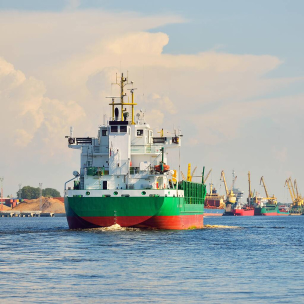 Velká zelená loď na přepravu volně loženého nákladu přijíždí do nákladového terminálu při západu slunce. Lodě a jeřáby v pozadí. Dramatická oblačnost. Nákladní doprava, globální komunikace, průmysl, ekonomika, logistika - Fotografie, Obrázek