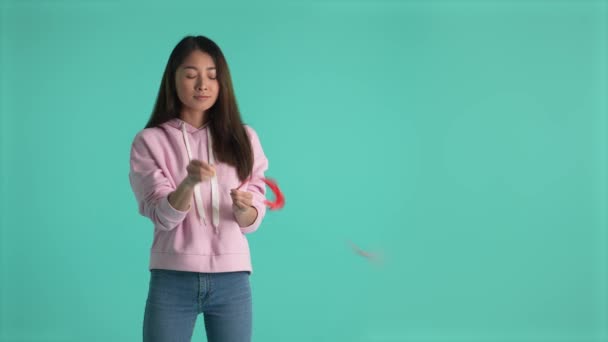 Upset young woman piercing red balloon with needle feeling lonely on Birthday. Sad asian female expressing bad mood and loneliness on holidays isolated against blue studio background - Footage, Video