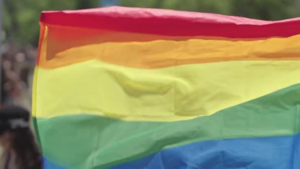 Die LGBTQ-Regenbogenfahne weht in Zeitlupe mit Menschen im Hintergrund - Filmmaterial, Video