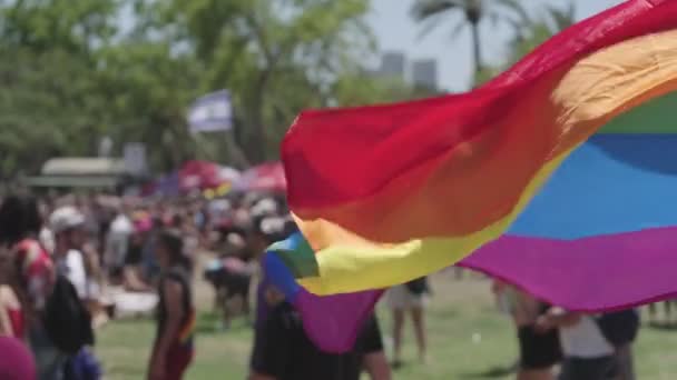 La bandera del arco iris LGBTQ ondeando en cámara lenta con la gente en un segundo plano - Metraje, vídeo