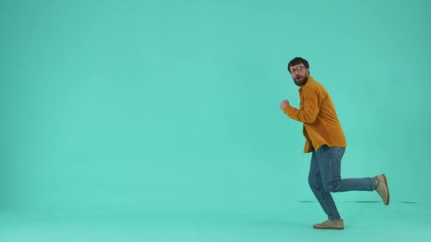 Side view of funny bearded guy showing hurry and tardiness while running and looking at wrist watch isolated over blue background. Male shopaholic rushing to discounts and sales - Footage, Video