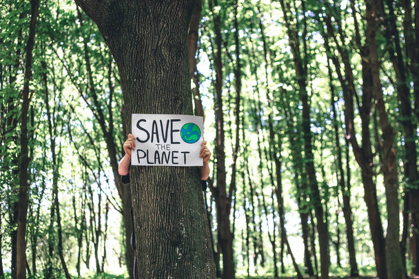 Plakat im Aufruf zur Rettung des Planeten in weiblichen Händen im Wald, das Konzept der Pflege der Natur, Reinigung, Recycling und Ökologie. - Foto, Bild