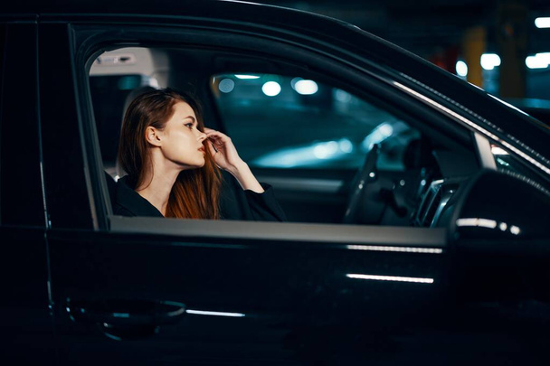 vízszintes fénykép oldalról, éjjel, egy fekete autóban ülő nőről, aki elgondolkodva várja, hogy a kezét az arcához szorítsa. Kiváló minőségű fénykép - Fotó, kép