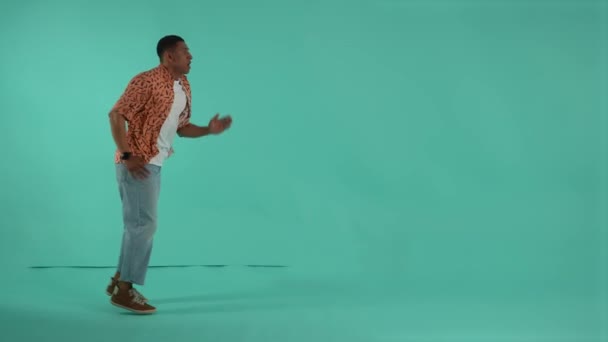 Expressive dark-skinned man running on same spot pretending to be in a hurry. Man looking at wrist watch and speeding up to not be late for discounts or sales, studio shot isolated on background - Footage, Video