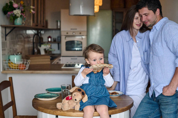 Mom, dad and daughter eat together in the kitchen. Happy family concept. - 写真・画像