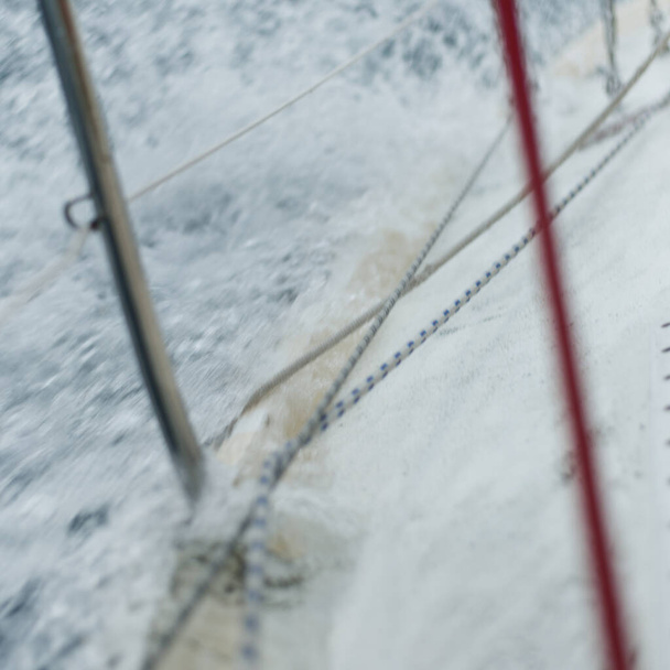 Heeled yacht sailing in an open sea. View of the deck and rigging equipment. Dark storm waves, water splashes. Long exposure, motion. Rough weather, cyclone, danger. Regatta, racing, sport - Zdjęcie, obraz