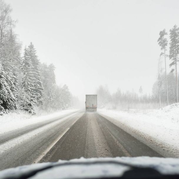 Leere Autobahn (Asphaltstraße) durch den verschneiten Wald, ländliche Gegend. Blick aus dem Auto. Europa. Natur, Weihnachtsurlaub, abgelegene Orte, Winterreifen, gefährliches Fahrkonzept - Foto, Bild