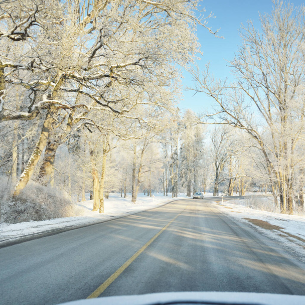 Leere Autobahn (Asphaltstraße) durch schneebedeckten Wald und Felder, ländliche Gegend. Schneeverwehungen. Europa. Natur, Weihnachtsurlaub, abgelegene Orte, Winterreifen, gefährliches Fahrkonzept - Foto, Bild