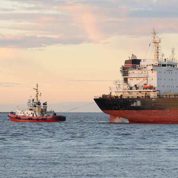Μεγάλο φορτηγό πλοίο φτάνει στο λιμάνι το ηλιοβασίλεμα. Βαλτική θάλασσα. Μεταφορές εμπορευμάτων, ναυτικά σκάφη, παγκόσμιες επικοινωνίες, εφοδιαστική, ναυτιλία, παράδοση, βιομηχανία, εμπόριο, οικονομία - Φωτογραφία, εικόνα