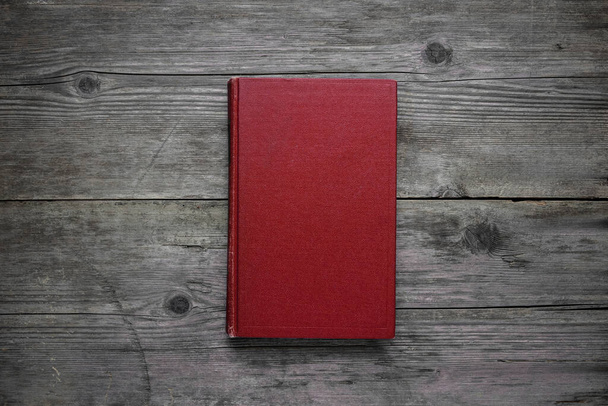 A closed book on an old wooden table. Red hard cover. Vintage background. - Foto, Imagem