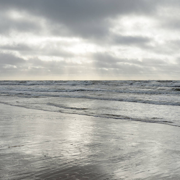 Πανοραμική θέα της Βαλτικής θάλασσας από την αμμώδη ακτή (αμμόλοφοι). Δραματικός ουρανός με λαμπερά σύννεφα. Κύματα, πιτσιλιές νερού. Ειδυλλιακή θαλασσογραφία. Καιρός άνοιξη, κλιματική αλλαγή, φύση - Φωτογραφία, εικόνα