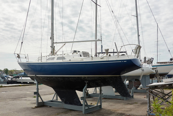 Blue sloop rigged sailboat standing on land in a yacht club. Service, repair, transportation, sport, recreation, leisure activity - Фото, изображение
