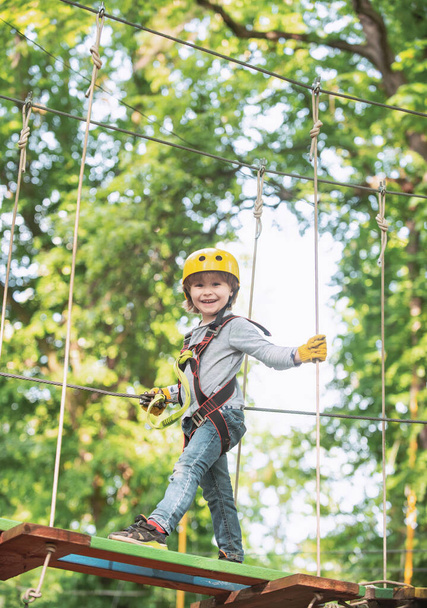 Toddler kindergarten. Active children. Balance beam and rope bridges. Toddler age. Cute child boy. Rope park - climbing center. Helmet and safety equipment - 写真・画像