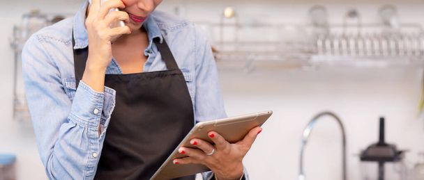 Young woman is barista talking on phone for order and using tablet computer and delivery online in the cafe, entrepreneur and small business, employee or owner retail, startup business concept. - Photo, image