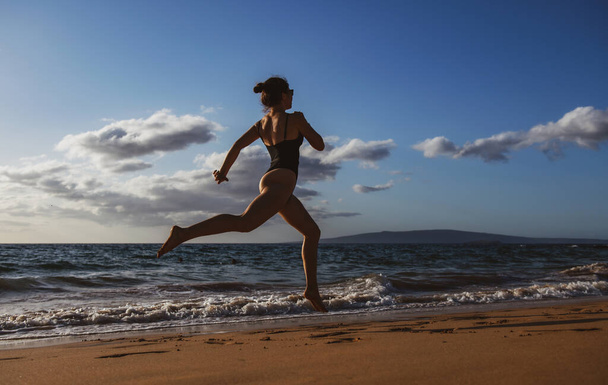 Woman running along ocean surf by water pool to keep fit and health. Woman fitness, jogging workout and sport activity on summer holiday - Valokuva, kuva